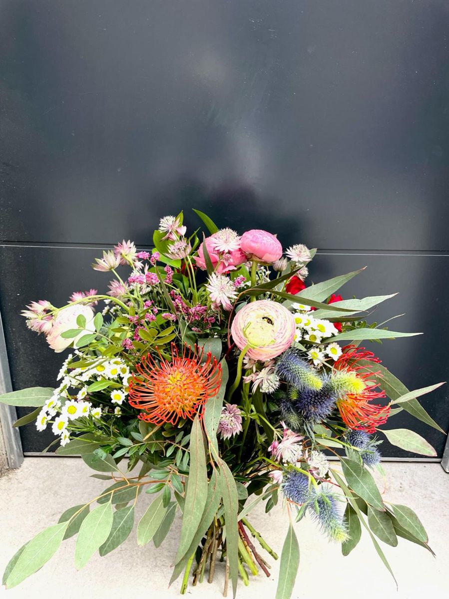 Ramo con protea naranja, cardo azul y flores rosas sobre fondo gris