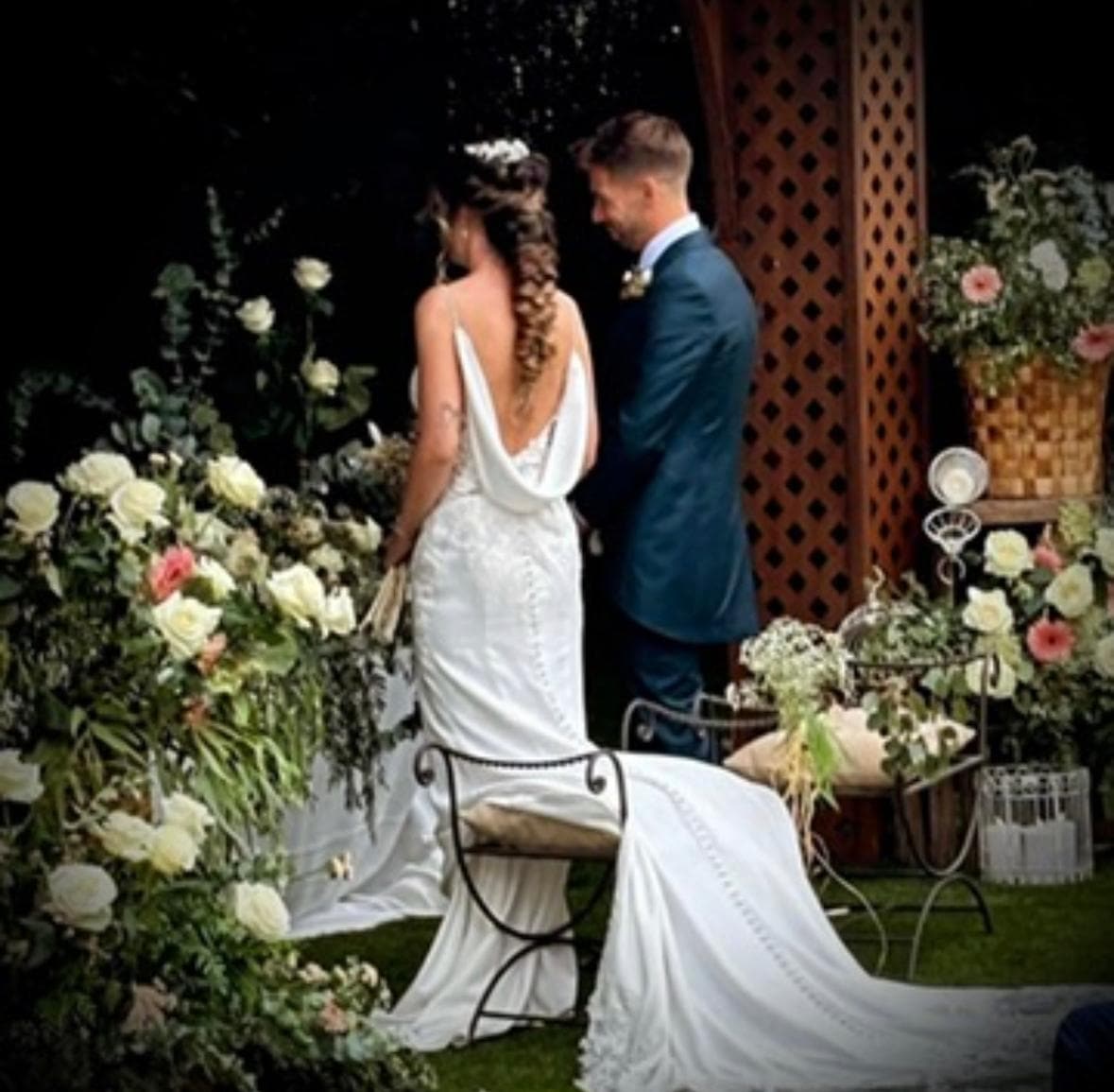 Novios de espaldas frente al altar de rosas blancas y verdor de su boda