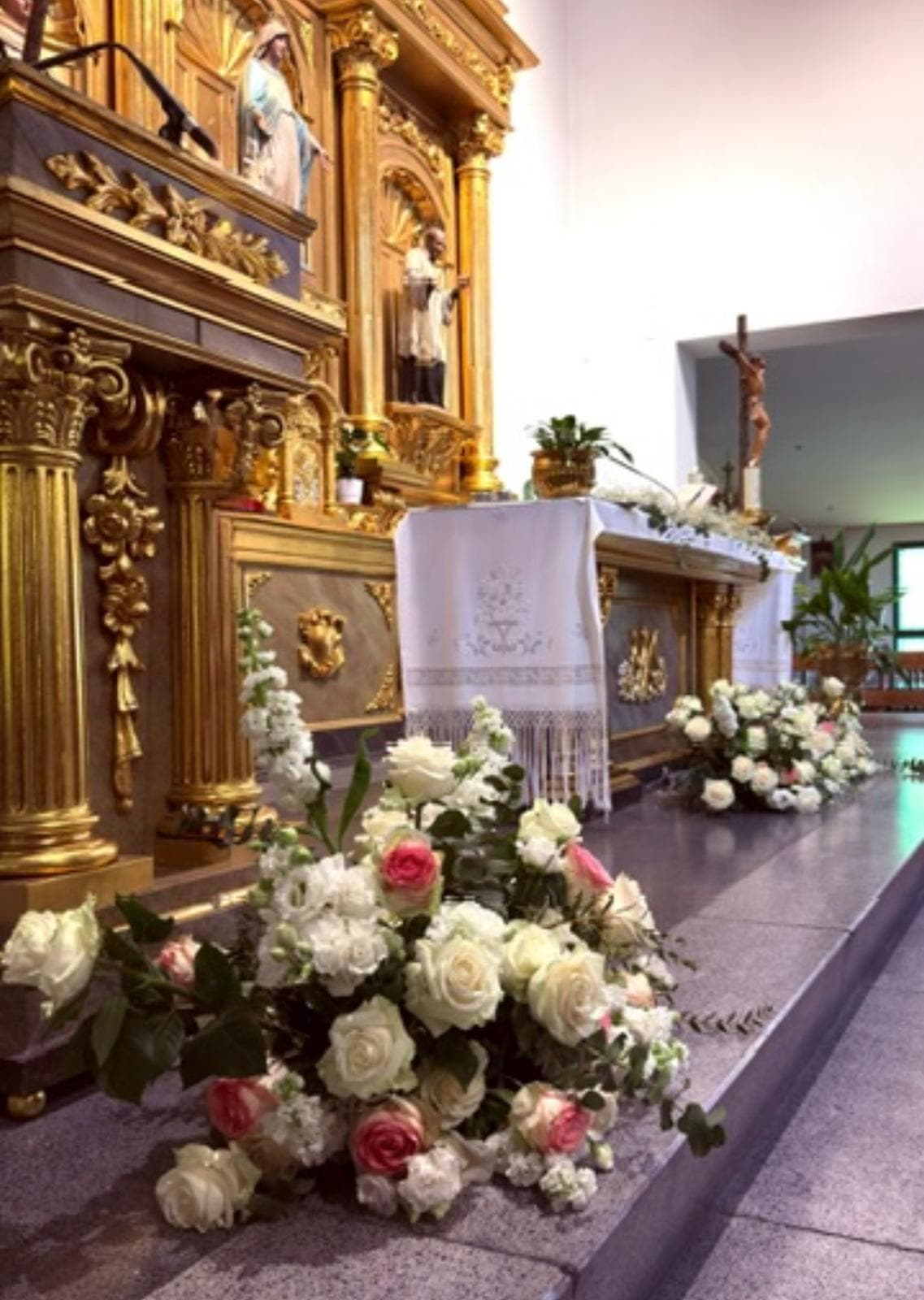 Rosas blancas y rosadas a los pies de un altar dorado de iglesia