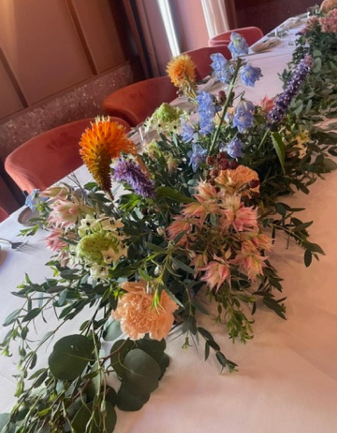 Camino de mesa con kniphofia naranja, delphinium azul y flores exóticas
